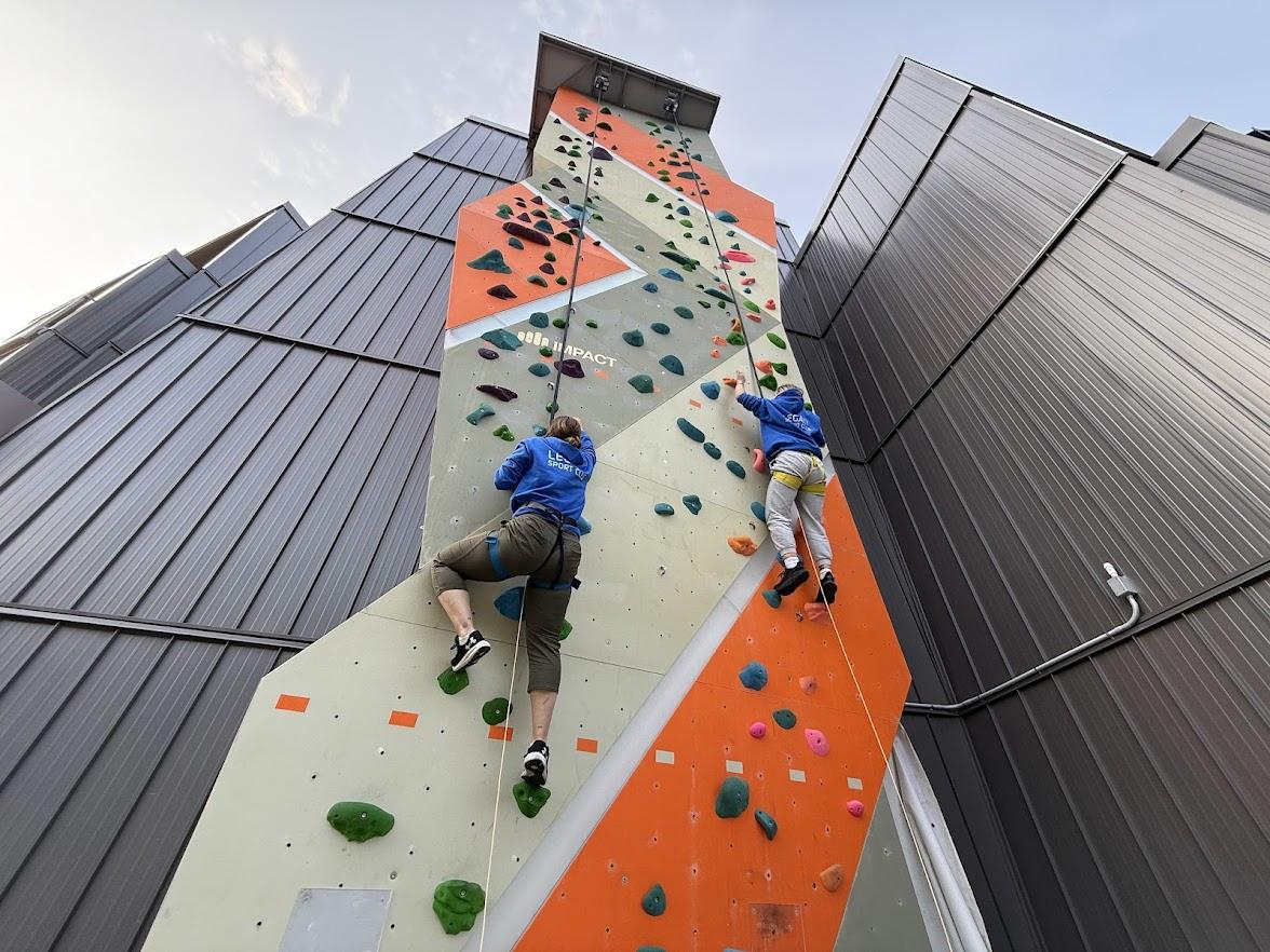 Two people climbing a tall outdoor rock wall.
