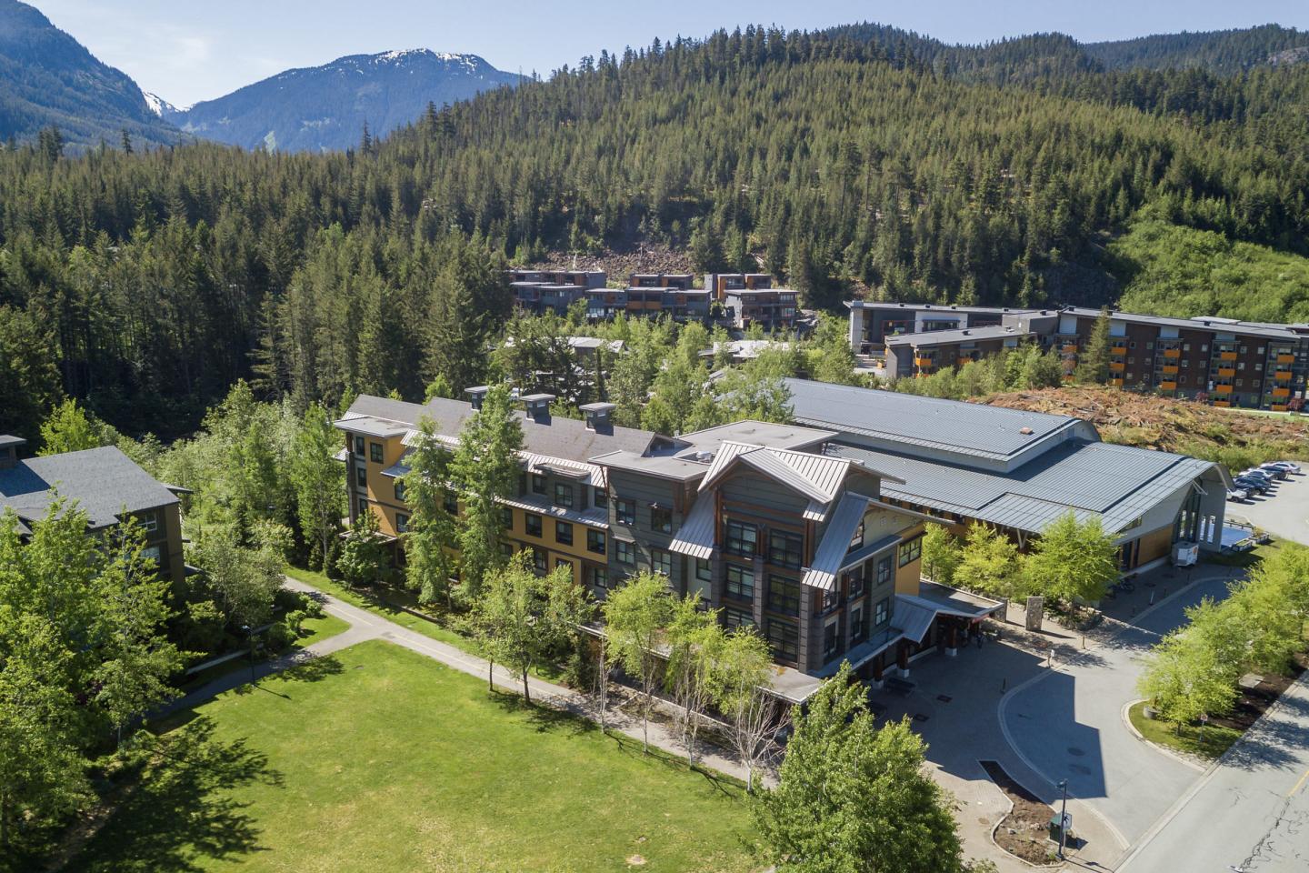 Aerial view of a lodge surrounded by trees and mountains under a blue sky.