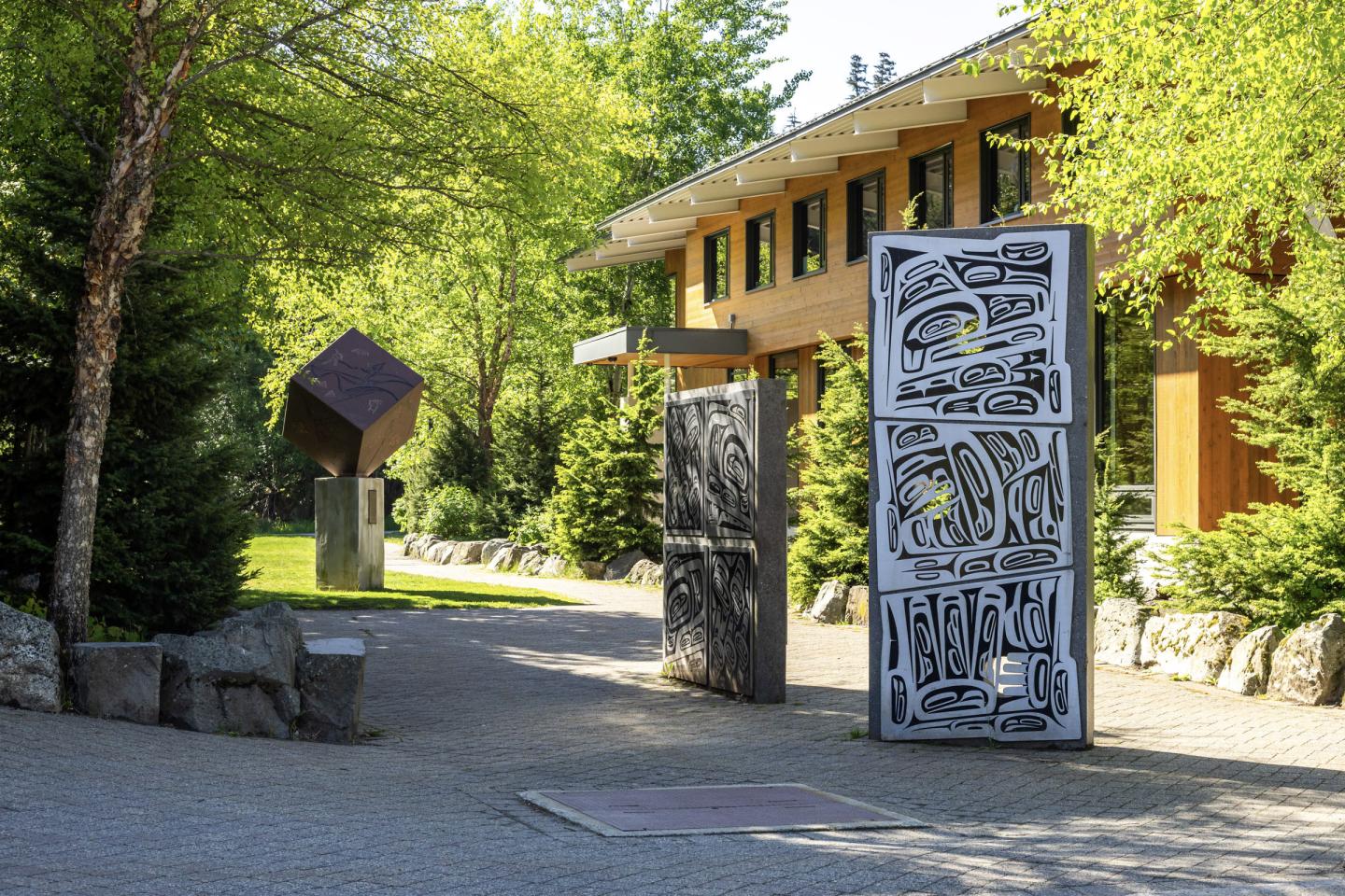 Sculpture garden with abstract metal pieces, sunny woodland setting.